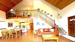 Un amplio salón con una escalera de madera, una mesa de comedor con sillas, un sofá de cuero y una pequeña mesa auxiliar.