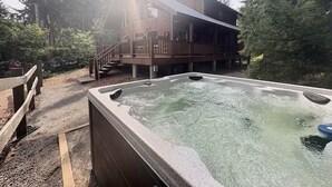Una cabaña de madera con jacuzzi y terraza, rodeada de árboles.