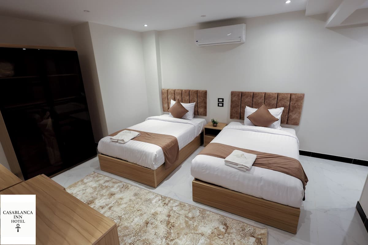 A hotel room with two beds, a wardrobe, a TV, and a small table.