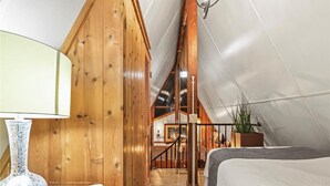 A cozy attic bedroom with wooden walls, a bed, a lamp, and a staircase leading to another room. - 3-bedroom cabin in gorgeous Clermont with AC (Clermont)