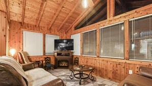 A cozy wooden cabin interior with a fireplace, leather furniture, and large windows. - 3-bedroom cabin in gorgeous Clermont with AC (Clermont)