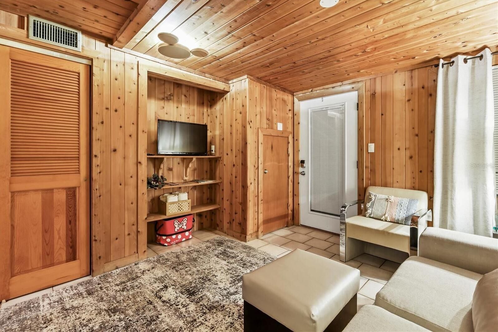 Habitación con paneles de madera, un televisor, un sofá y una puerta que da a un baño.