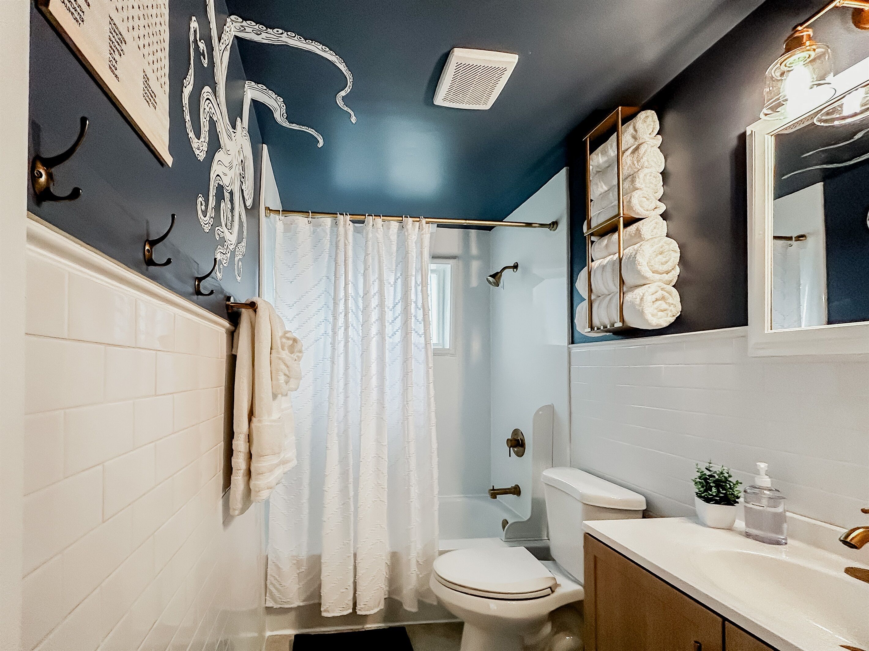 A bathroom with a white toilet, a shower curtain, a towel rack, a sink with a mirror, and a wall-mounted towel rack.