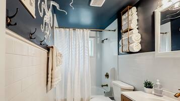 A bathroom with a white toilet, a shower curtain, a towel rack, a sink with a mirror, and a wall-mounted towel rack.