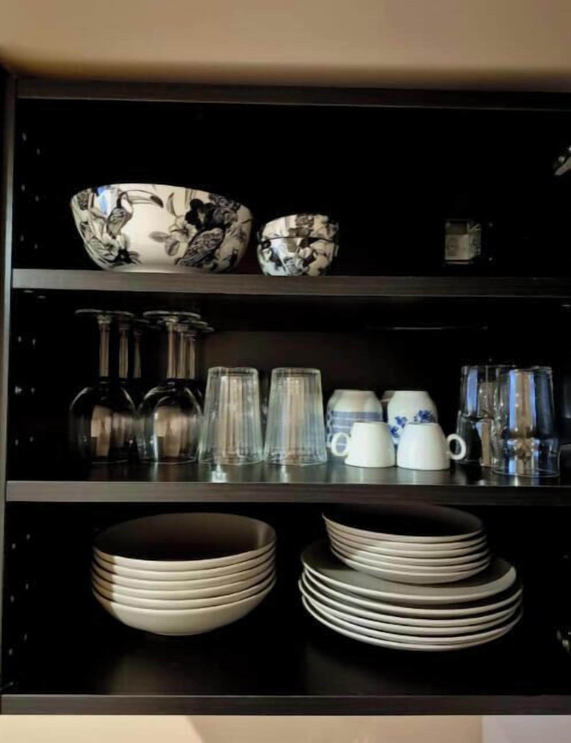 Una cocina con estantes negros que albergan diversos utensilios de cocina, como cuencos, platos y cristalería.