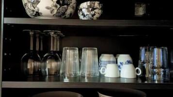 Ett kök med svarta hyllor där olika köksredskap förvaras, bland annat skålar, tallrikar och glas.