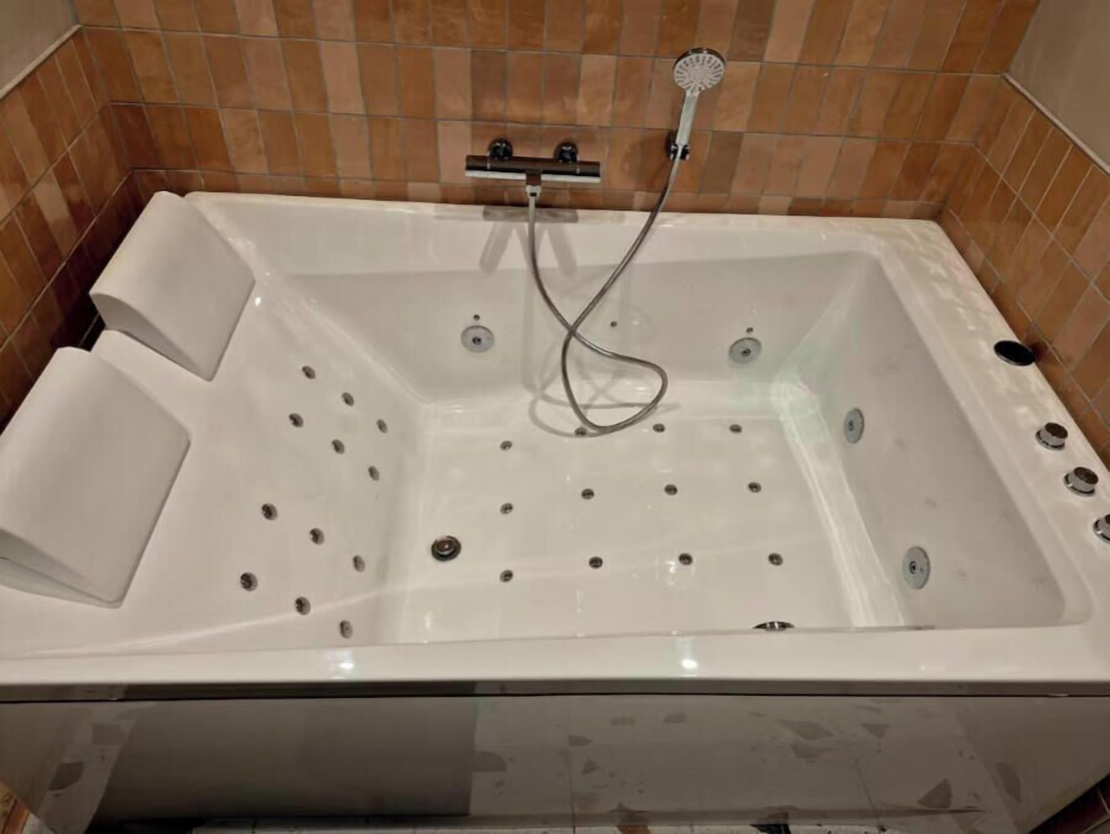 A white bathtub with a handheld showerhead, set against a tiled wall.