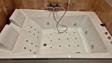 A white bathtub with a handheld showerhead, set against a tiled wall.