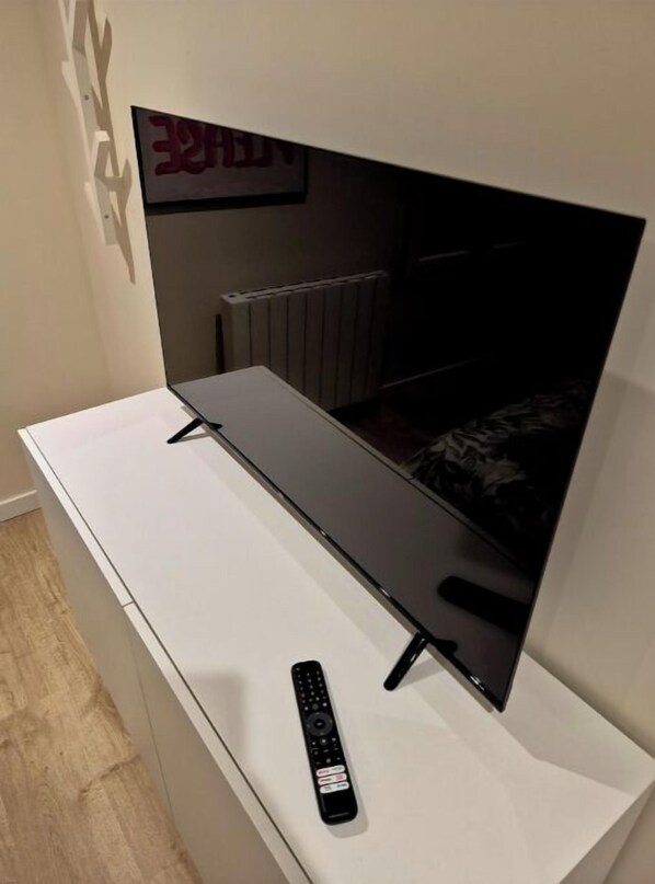 Un téléviseur à écran plat fixé sur un meuble blanc, avec une télécommande posée sur le dessus du meuble.