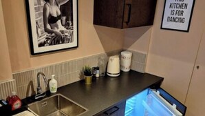 Et køkken med en stålvask, bordplade, køleskab og et skilt med teksten "THIS KITCHEN IS FOR DANCING".