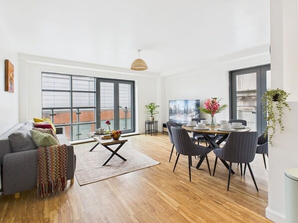 A modern living room with a sofa, dining table, and chairs, large windows, and a view of the city.