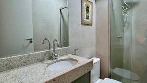 Un bagno con lavabo su piano in granito, un water, box doccia in vetro e una cornice con un'immagine appesa al muro.