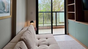 Un soggiorno moderno con un divano spazioso, una televisione a destra e un balcone affacciato su alberi.