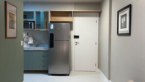 Una cucina moderna con un frigorifero in acciaio inox, un forno a microonde e una macchina del caffè. Si nota una porta bianca e un quadro appeso al muro.