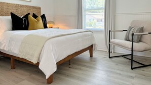 Ein Schlafzimmer mit einem hölzernen Bett, weißer Bettwäsche und Blick ins Grüne durch das Fenster.