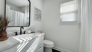 Een badkamer met een witte wastafel, een zwarte kraan, een wit toilet en een raam met jaloezieën.