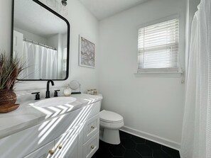 A bathroom with a white vanity, a black faucet, a white toilet, and a window with blinds. - Modern Home Near Beach & City Dog Friendly (Savannah)