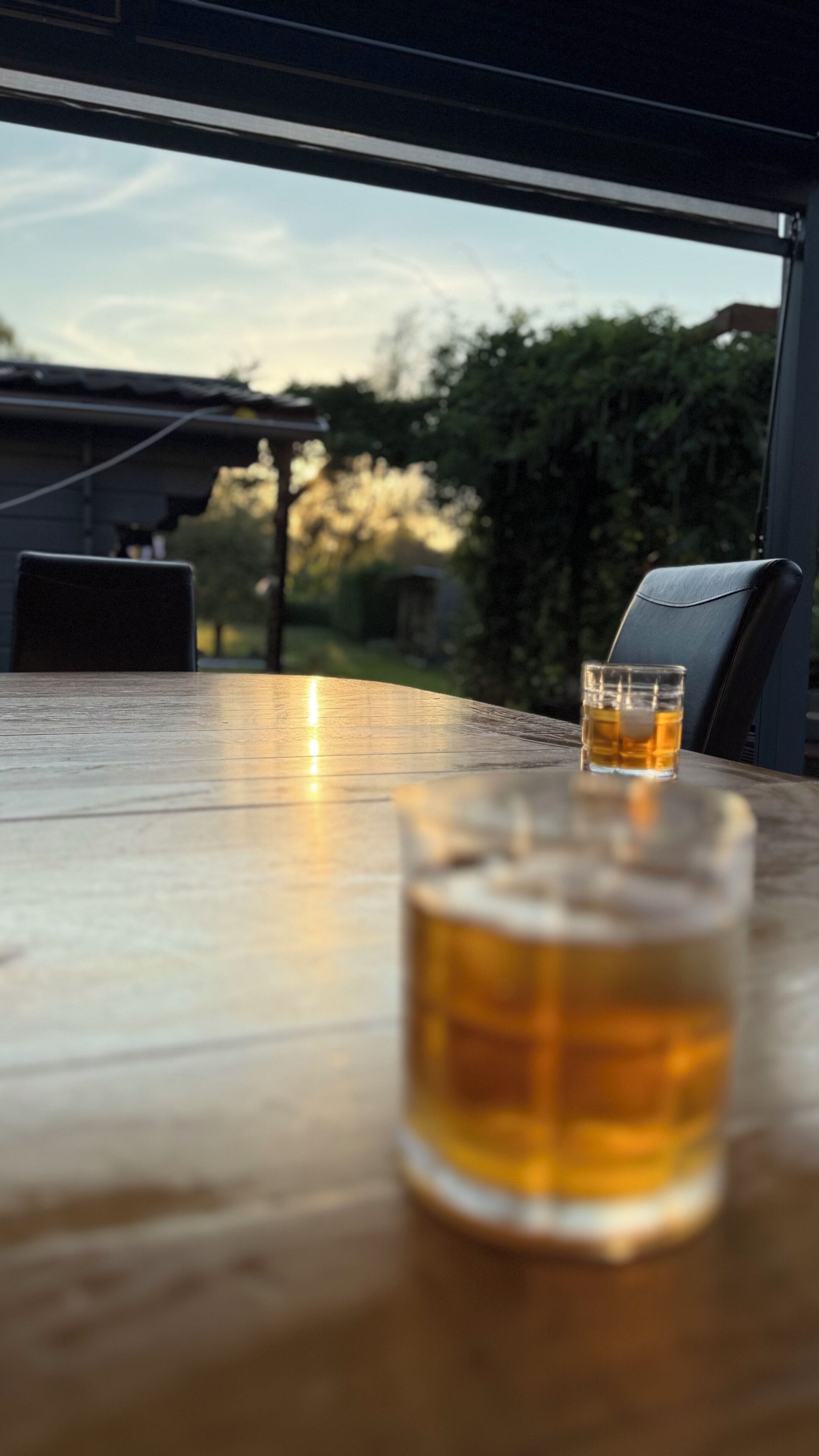 A wooden table with two glasses of amber liquid, likely beer, and a chair.