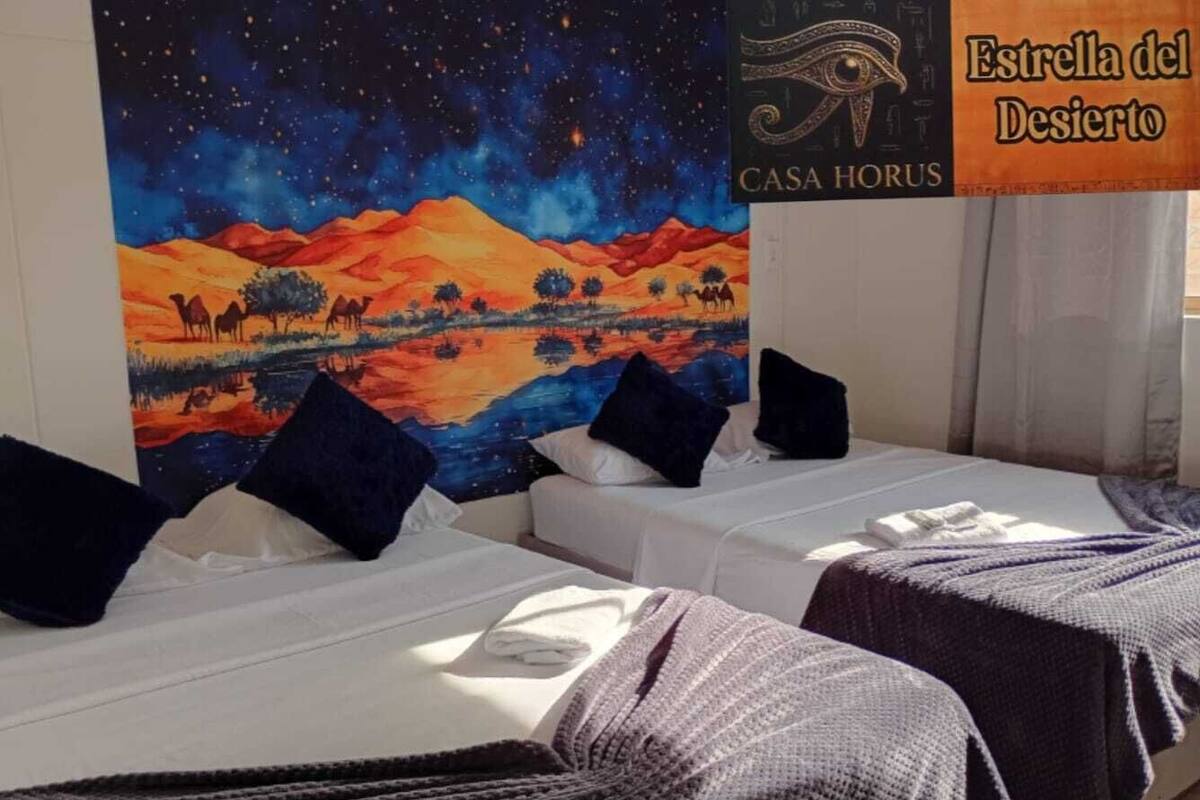 Ein Hotelzimmer mit zwei Betten, einem Sternenhimmel-Gemälde an der Wand und einem Schild mit der Aufschrift 'Estrella del Desierto CASA HORUS'.