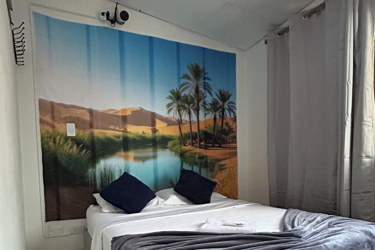 Ein Schlafzimmer mit Bett, Wandbild, Deckenleuchte und einem fenster mit Vorhängen.