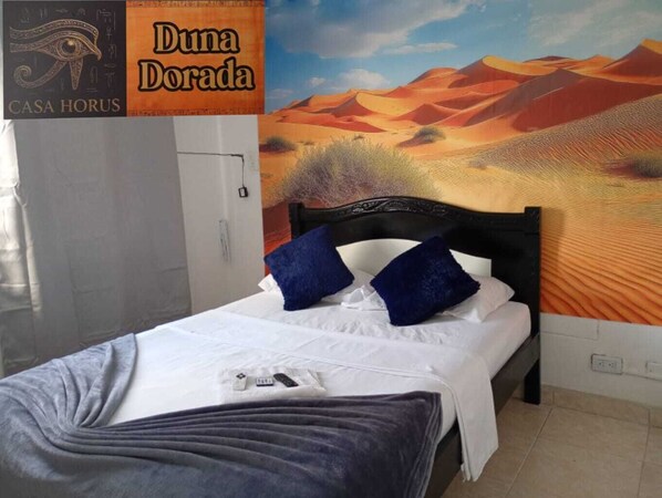 A hotel room with a bed, a nightstand, and a wall mural of a desert landscape.