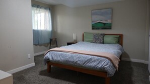 A bedroom with a bed, a nightstand, a lamp, a window with curtains, and a painting on the wall. - Bright Arvada Townhome with Backyard, Walkable to Old Town Arvada (Arvada)