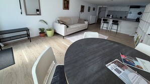 Ein modernes Wohnzimmer mit einer Couch, einem Esstisch und einer Küche im Hintergrund.