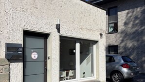 Ein Gebäude mit strukturierter Fassade, eine Tür mit einem Schild und ein geparktes Auto.