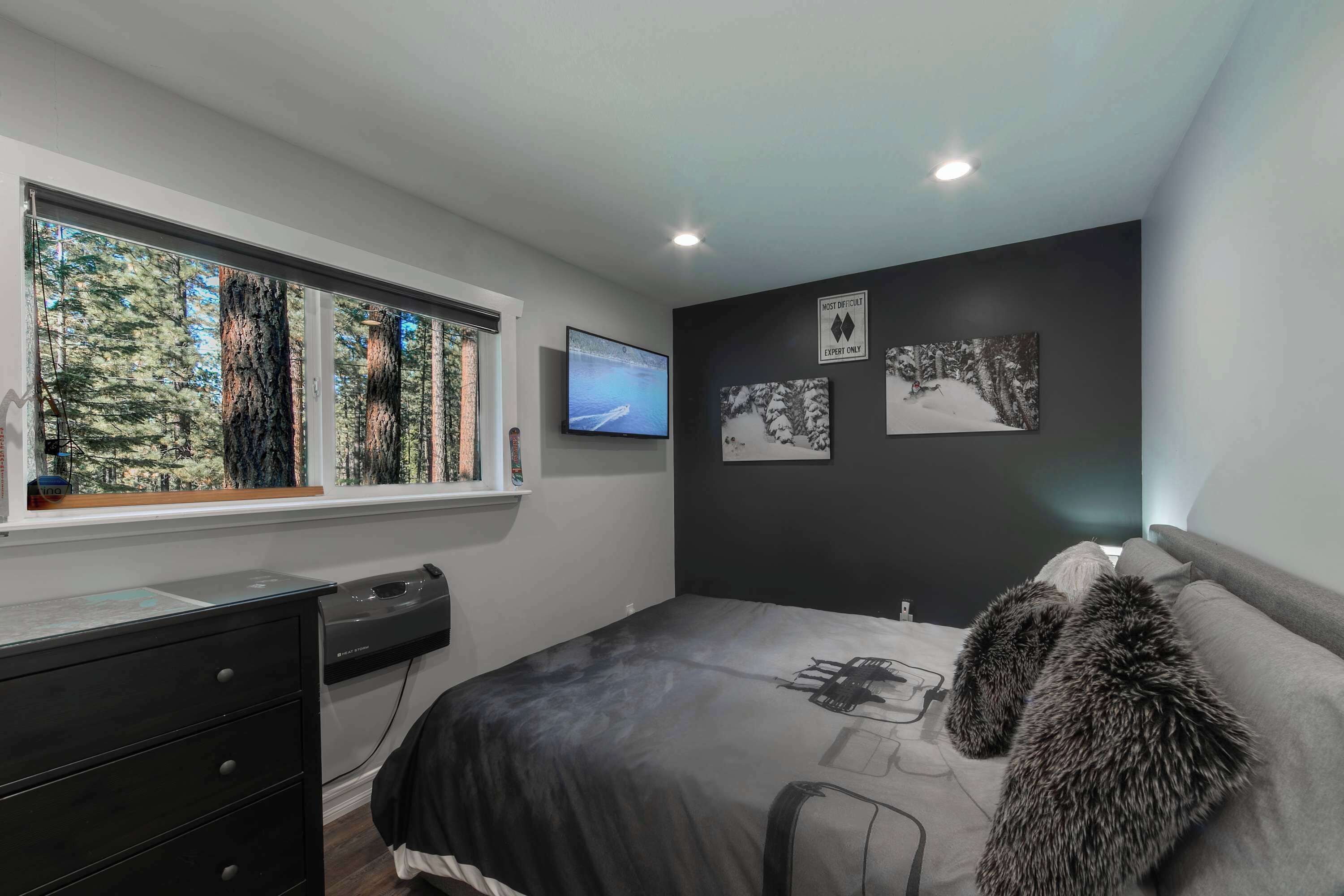 A bedroom with a large window, a bed with a fur throw, a desk with a computer, and artwork on the wall.