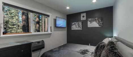 A bedroom with a large window, a bed with a fur throw, a desk with a computer, and artwork on the wall.