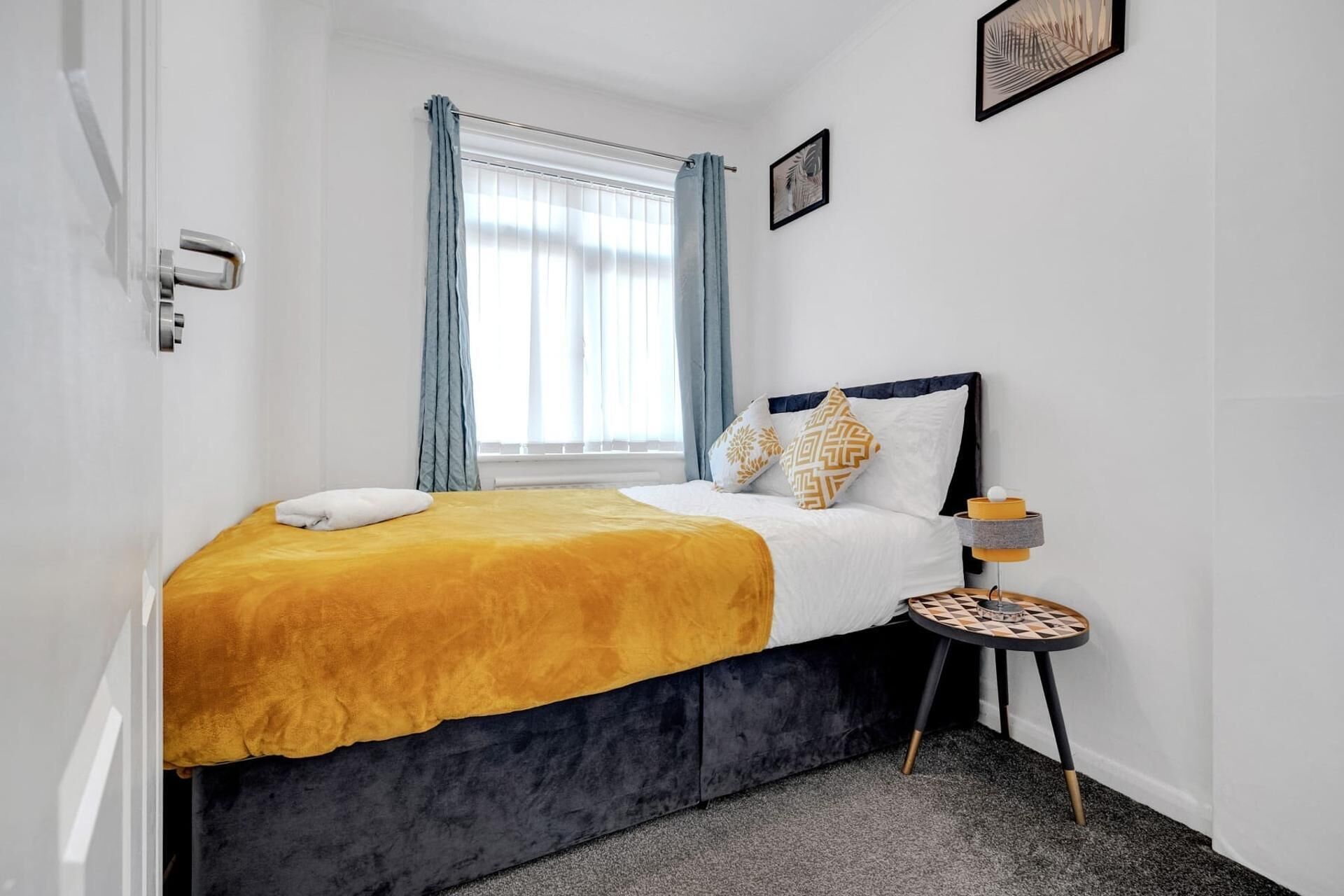 A hotel room with a bed, a bedside table, a window with curtains, and a wall-mounted picture.