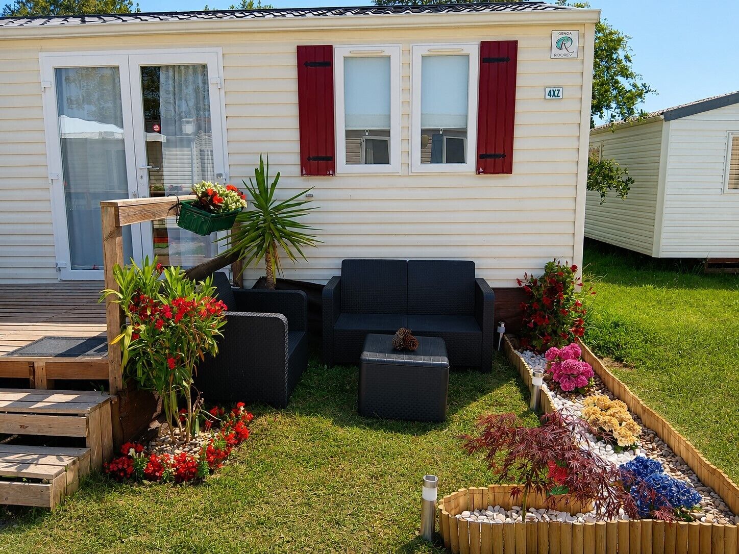 Une maison mobile dotée d’un patio aménagé avec du mobilier d’extérieur, d’un petit jardin avec différentes plantes et d’un ciel dégagé.