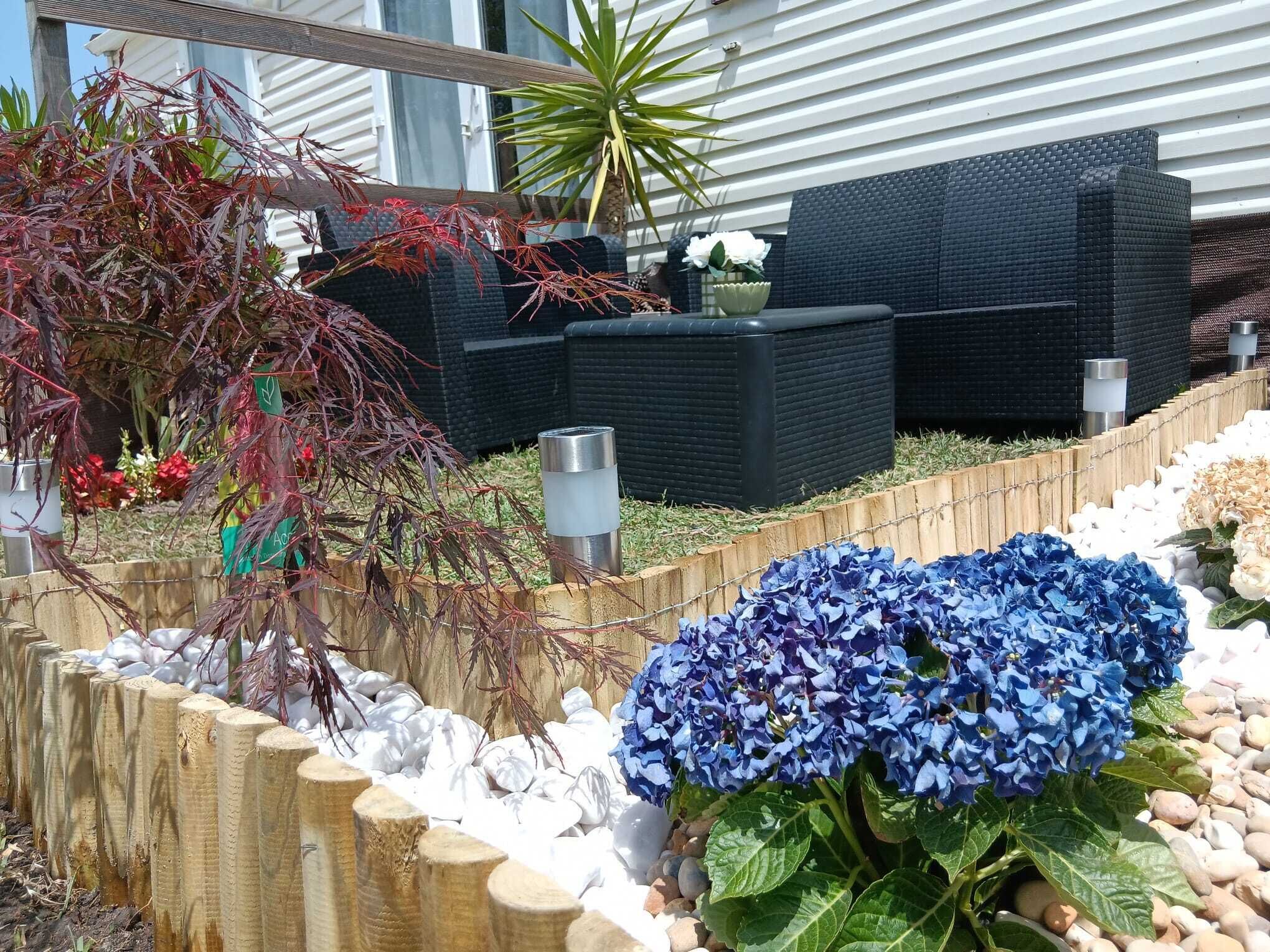 Ein Garten mit Holzzaun, einem schwarzen Outdoor-Sofa und einem blauen Hortensienstrauch.