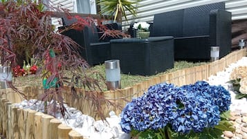 A garden with a wooden fence, a black outdoor sofa, and a blue hydrangea plant.