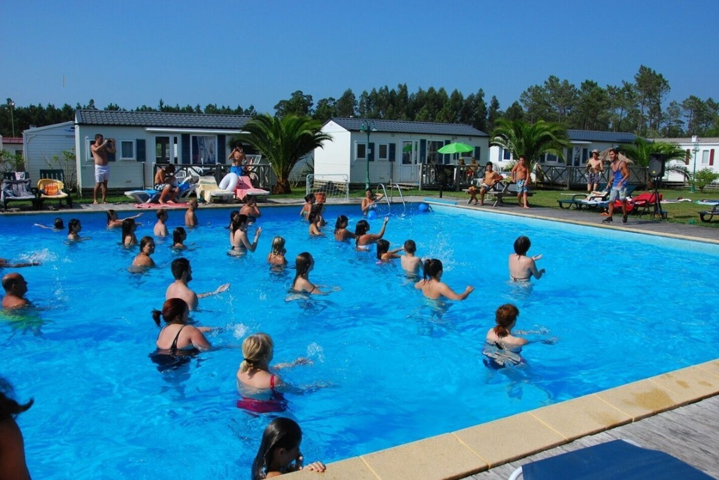 Ein Schwimmbecken mit darin badenden Personen, umgeben von Häusern und Palmen.