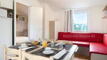 A dining area with a table set for two, a red sofa, and a view of the outdoors.