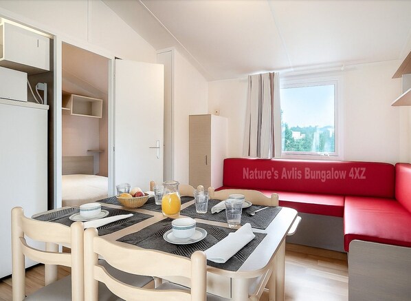 A dining area with a table set for two, a red sofa, and a view of the outdoors.