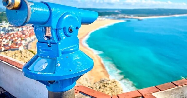 A blue telescope overlooking a beach with clear turquoise waters and a distant shoreline.