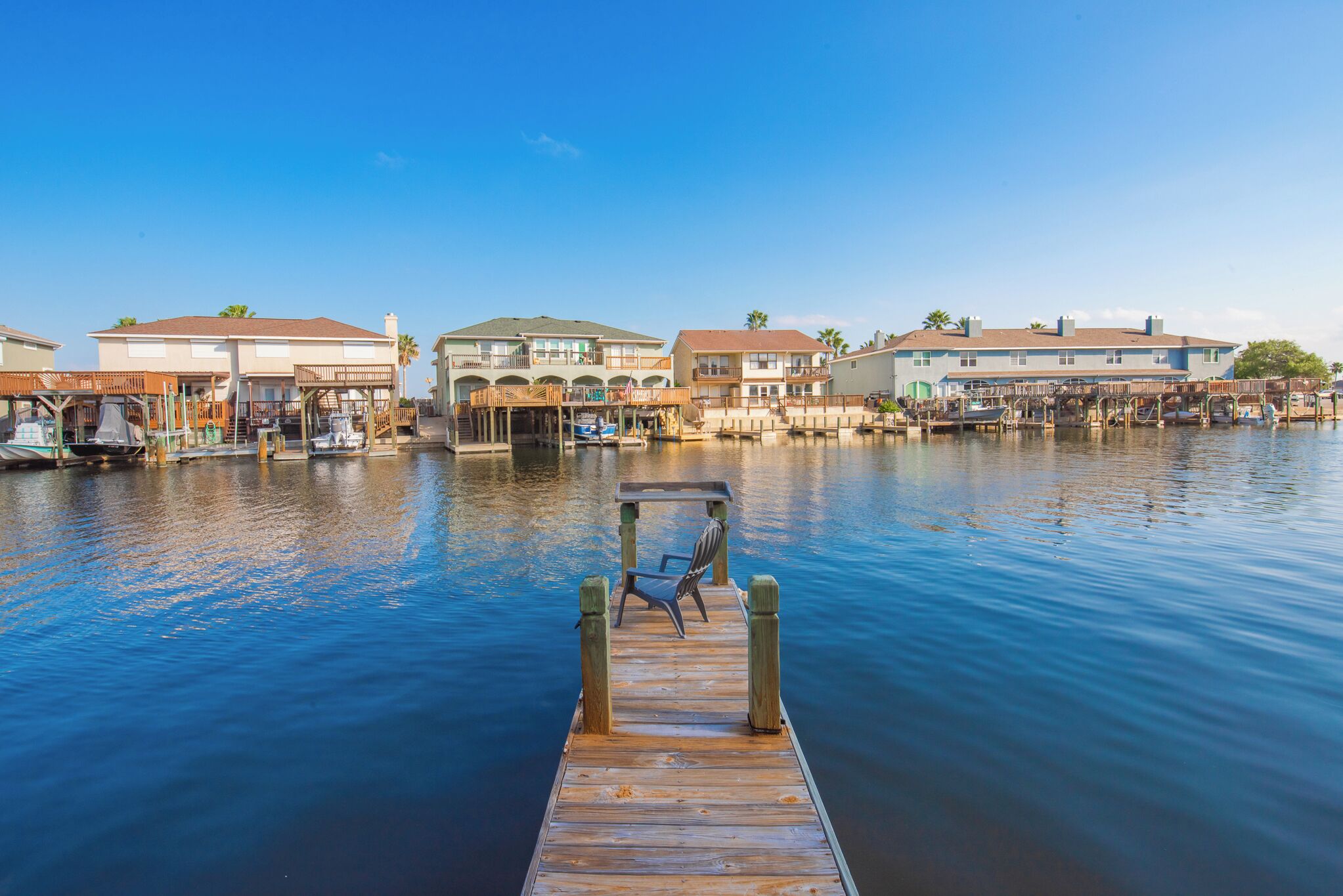 A wooden dock leading to a marina with boats, a chair, and buildings in the background.