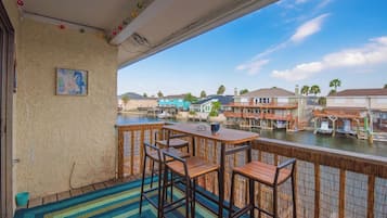 A balcony with wooden furniture, a view of a waterfront with buildings and boats, and a painting on the wall.