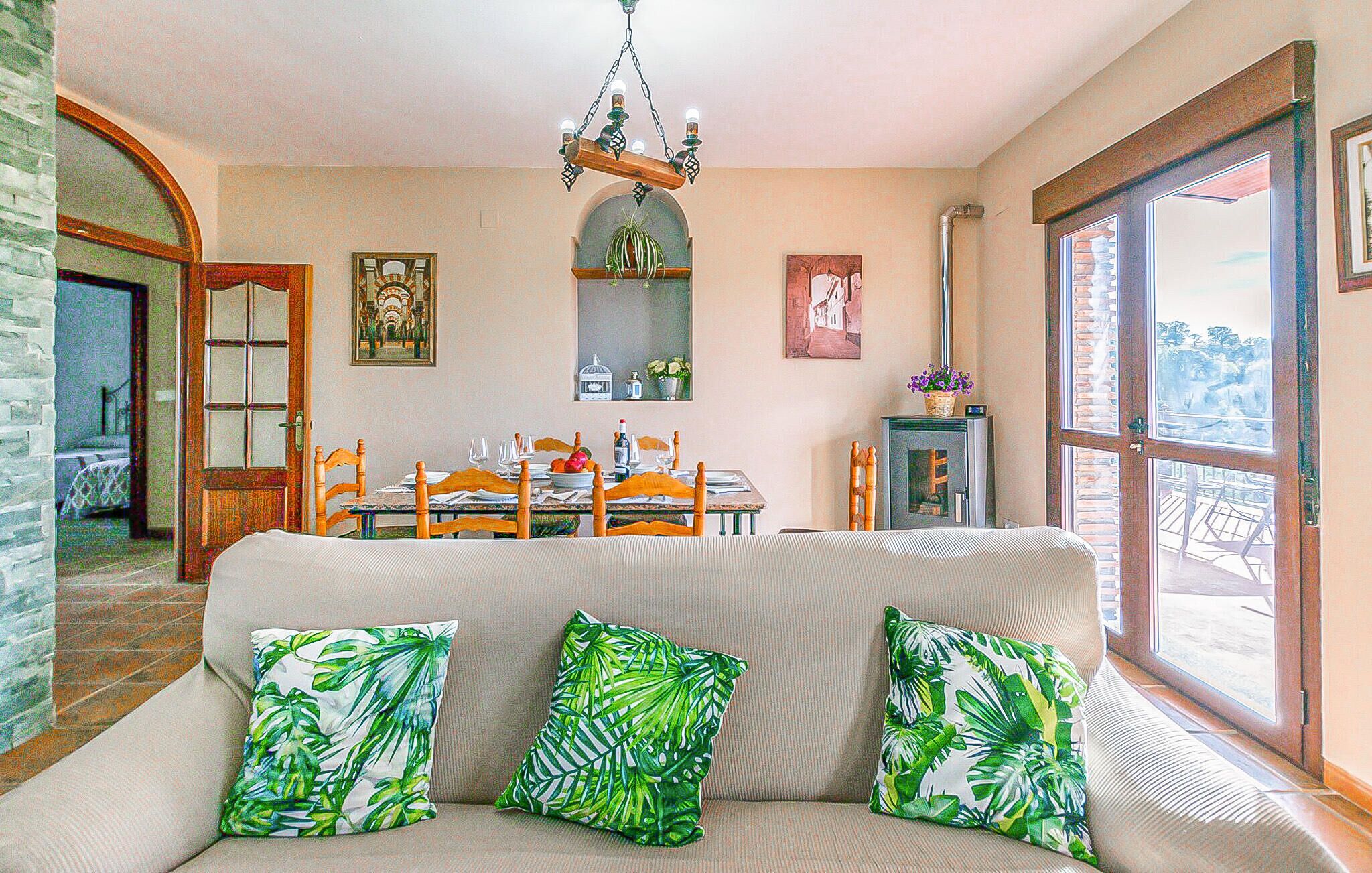Una sala de estar acogedora con un sofá, una mesa de comedor y sillas. Un candelabro cuelga del techo, y una ventana ofrece vistas al exterior.