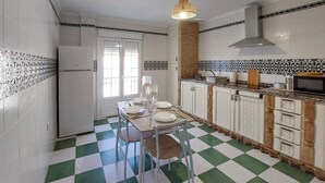 Une cuisine avec un carrelage à motifs, des meubles blancs, un mur d’accent en pierre et un luminaire suspendu.