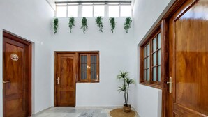Un couloir avec une porte en bois, une fenêtre dotée d’un panneau en verre dépoli et une plante en pot.