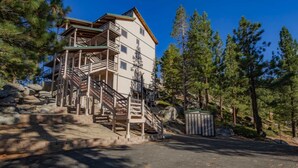 A multi-story building with a wooden staircase leading to a balcony, surrounded by trees and rocks. - Galaxy Way Close to Stagecoach Chair! (Stateline)