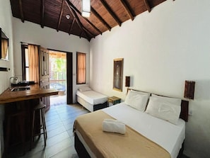 A room with a bed, a desk, and a small table. There is a window with curtains, a door, and a view of greenery outside. - Pousada da Praia Ferrugem (Garopaba)