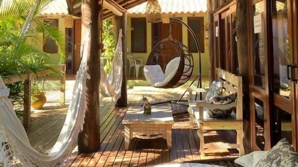 A wooden deck with a hammock, hanging chairs, and a bed. - Pousada da Praia Ferrugem (Garopaba)