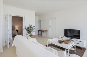 A modern, white-themed living room with a sofa, a TV, a coffee table, and a potted plant.