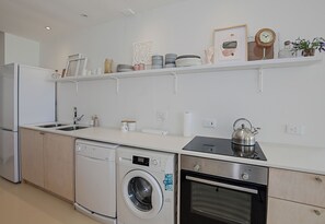 A modern kitchen with a dishwasher, washing machine, oven, and a kettle on the countertop.