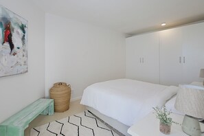 A bedroom with a bed, a bench, a large woven basket, and a painting on the wall.