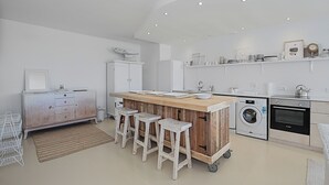 Une cuisine moderne dotée d’un îlot central, de tabourets de bar, d’un lave-linge et d’un four encastré.